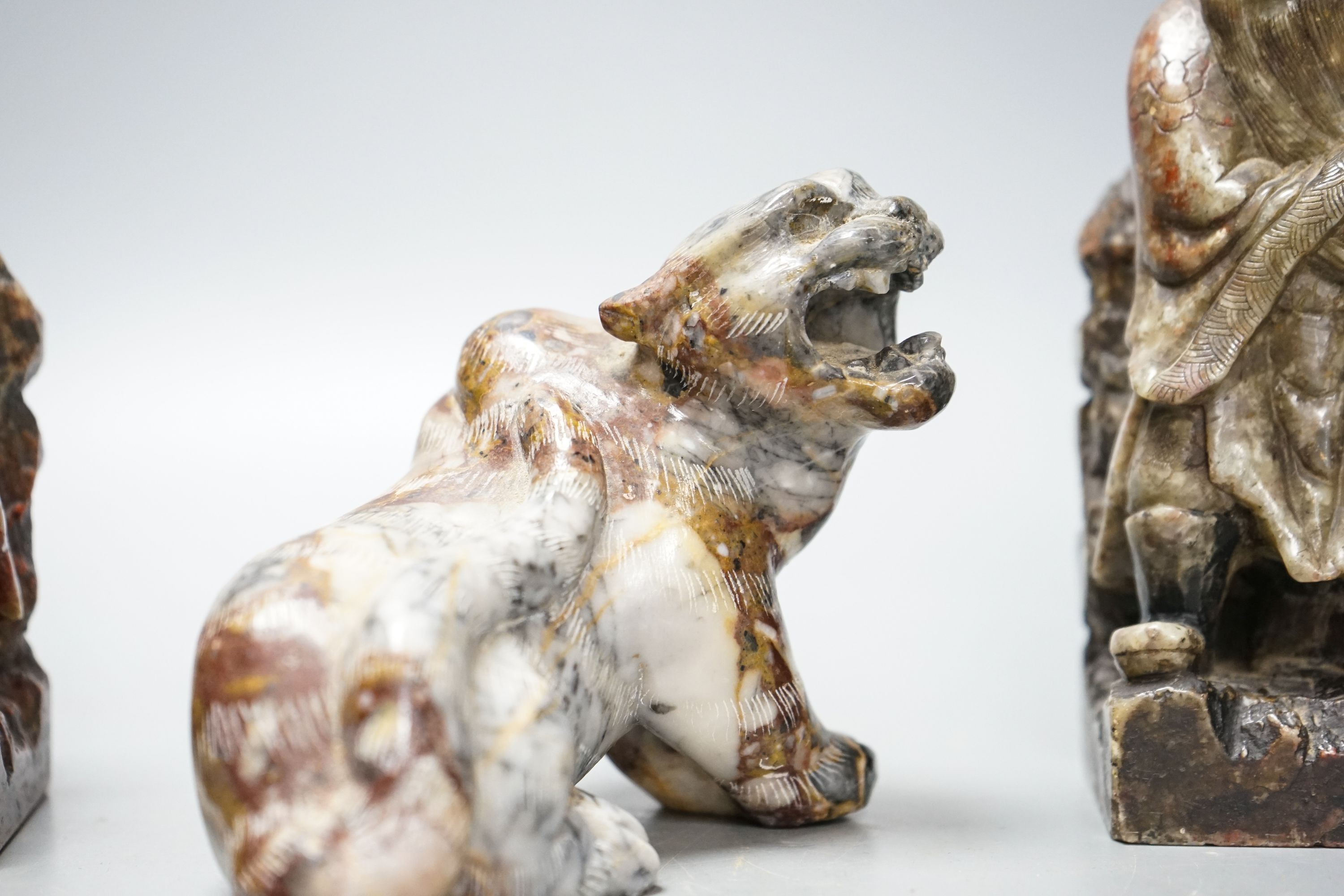 A pair of Chinese soapstone figures of immortals, modelled seated on rocky bases and a similar figure of tiger, 12cm